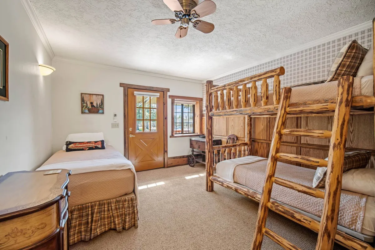 A family-friendly bedroom featuring a bunk bed and a single bed, with warm wooden furniture and a view through the window. The cozy setup radiates playfulness and comfort, perfect for children or families seeking a relaxing stay together.