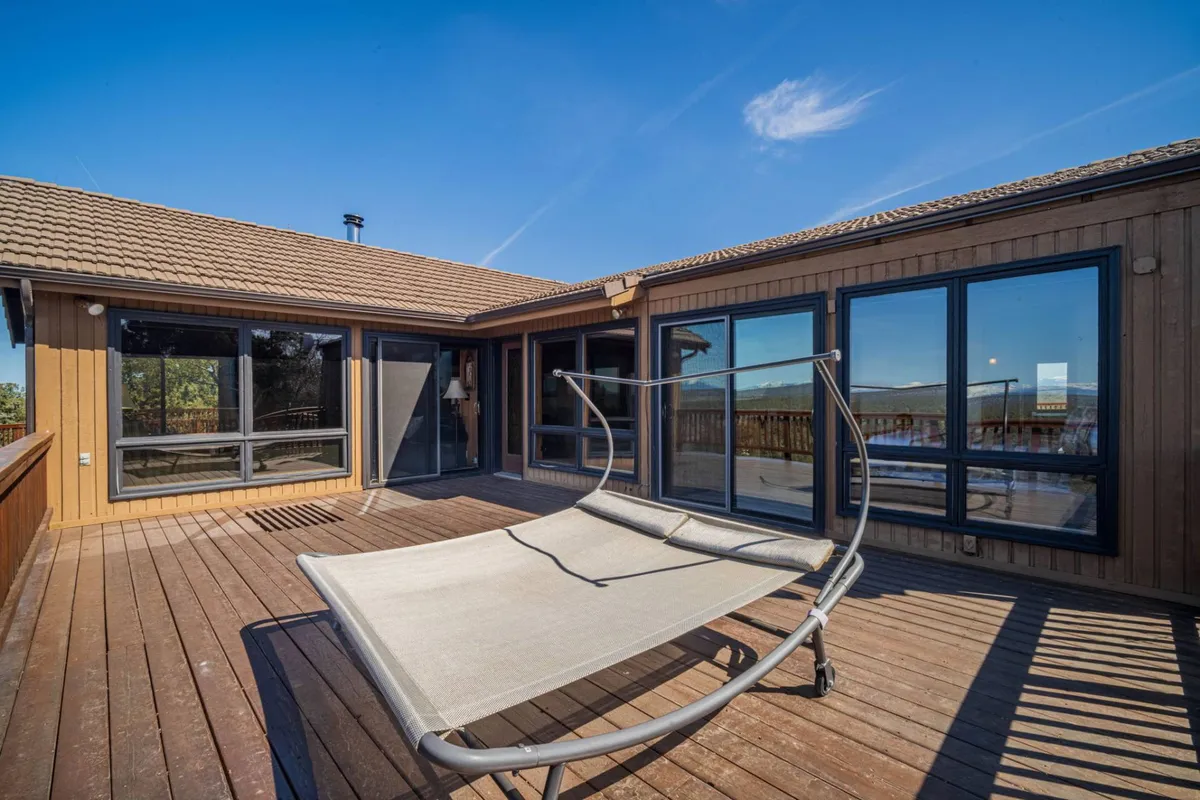 This image showcases a tranquil wooden deck with a hammock, large windows, and panoramic views of the surrounding natural landscape, inviting guests to relax outdoors and enjoy the scenery.