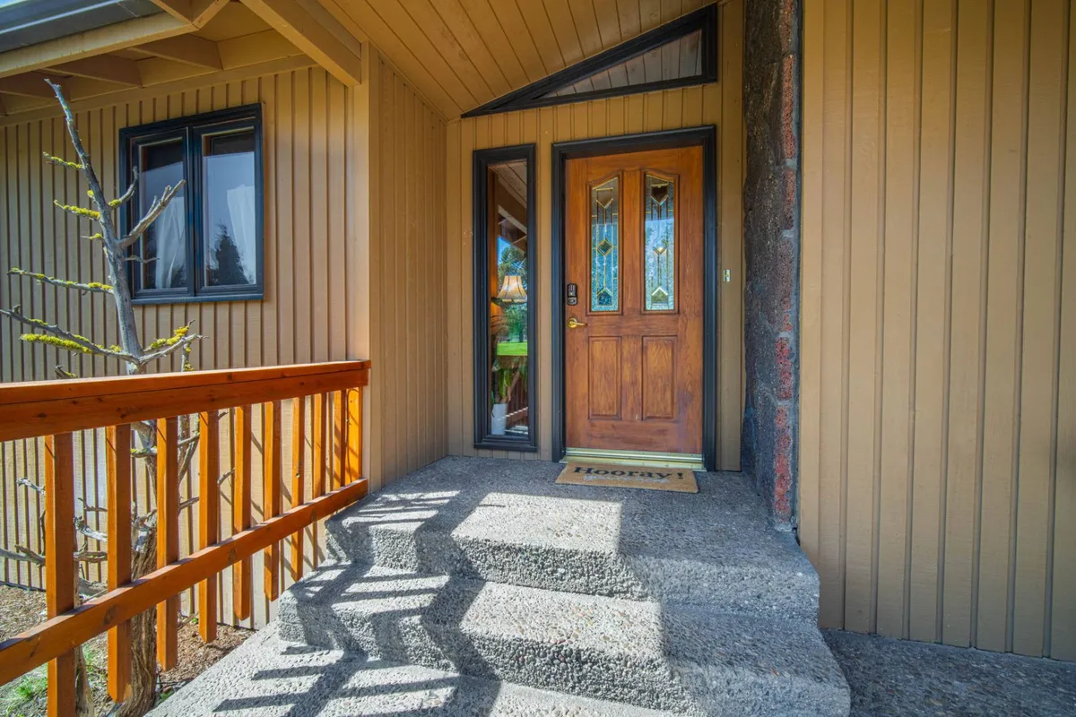 A welcoming exterior shot of the home's wooden front door, complete with a welcome mat, front steps, and a sturdy railing, set against the inviting outdoor surroundings.