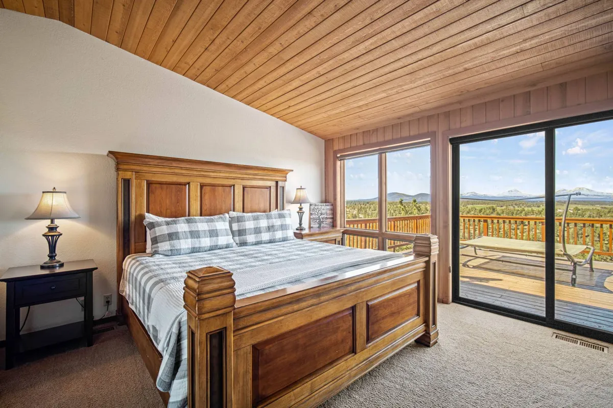 A restful bedroom with a wooden bed, expansive windows offering mountain views, and a nightstand with a lamp. The space is calm and bright, ideal for relaxation and enjoying the tranquil natural scenery outside.
